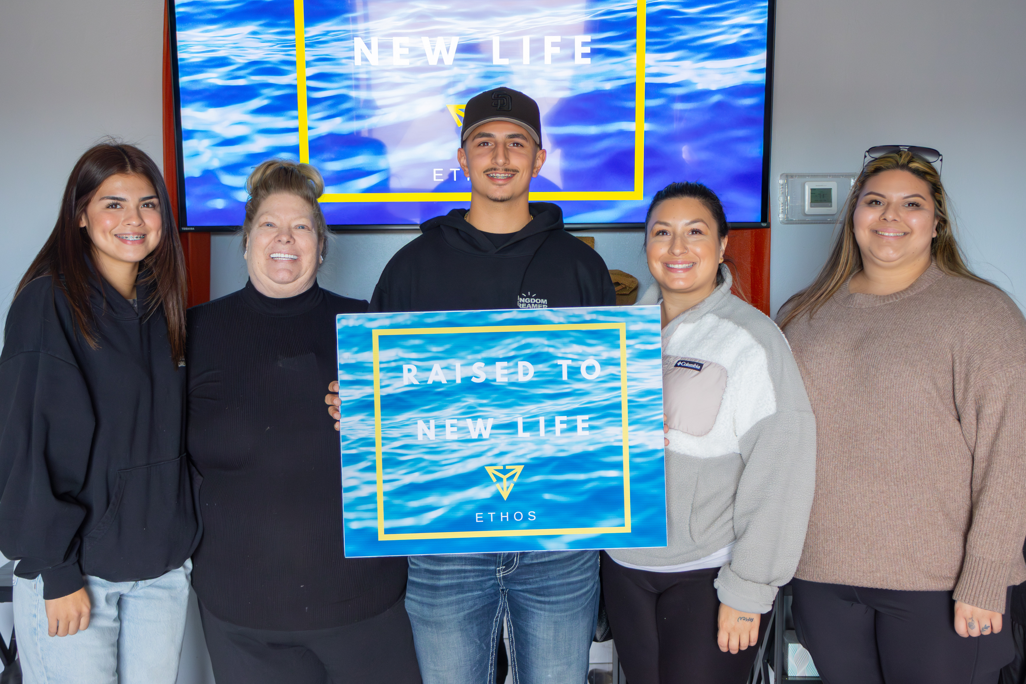 Baptism celebration at Ethos Church - group holding Raised to New Life sign