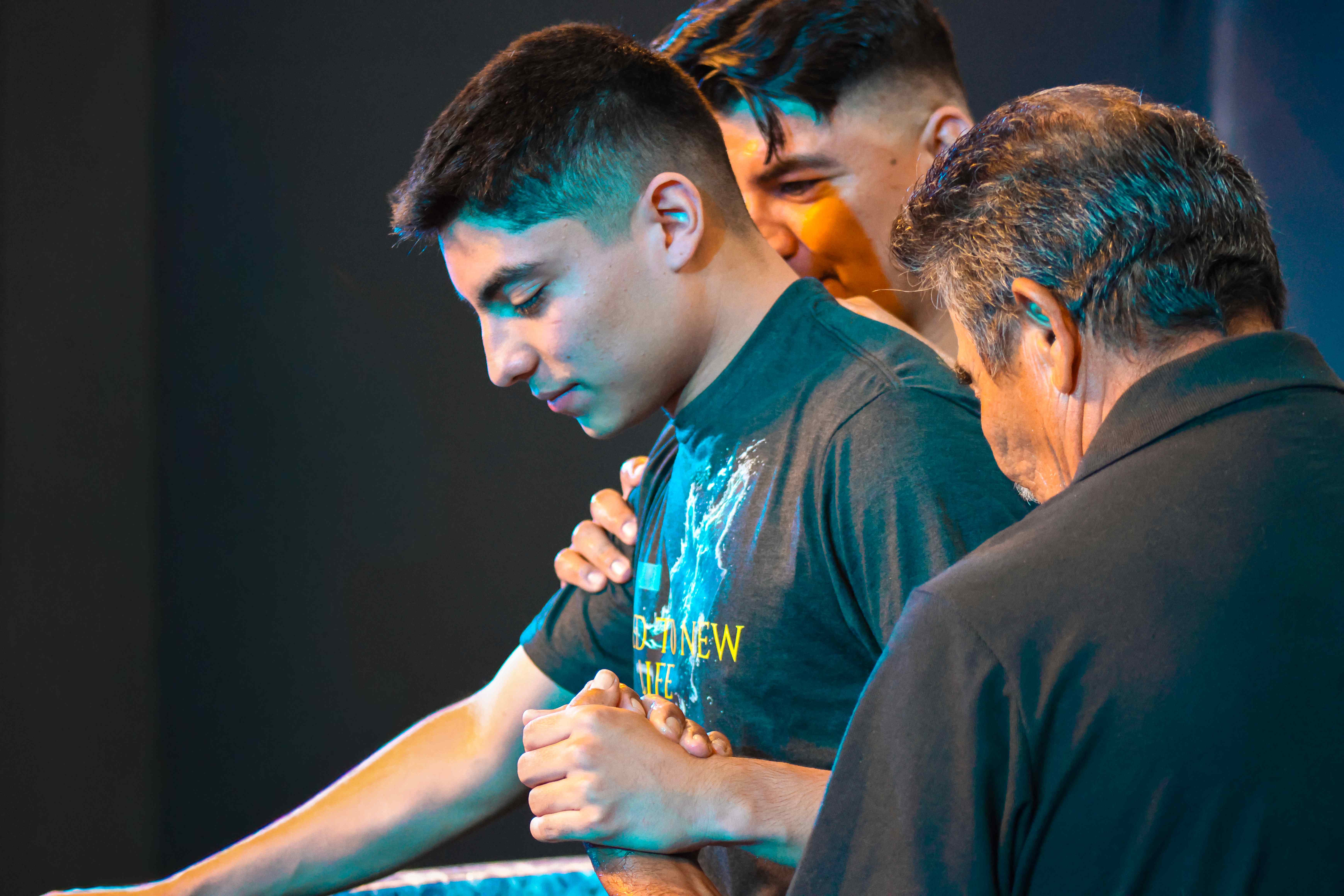 Newly baptized young man in a Raised to New Life shirt being prayed over at Ethos Church